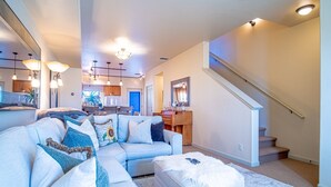 A spacious living room with a sectional sofa, ottoman, and a staircase leading to another level. - 2BD Sweetwater Condo - Community Park, Pool + Hot Tub (Hailey)