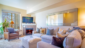 A living room with a fireplace, a television, and a large mirror. - 2BD Sweetwater Condo - Community Park, Pool + Hot Tub (Hailey)