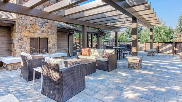 Eine Außenpatio mit Steinmauern, einem Kamin aus Stein, Korbmöbeln und einer Pergola.