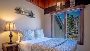 Una camera da letto con un letto grande, un comodino con una lampada, una finestra vista alberi e un soffitto in legno.