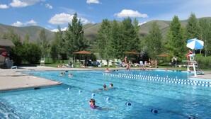 A swimming pool with multiple lanes, surrounded by lounge chairs and umbrellas, set against a backdrop of hills and trees. - 2BD Ranch Condo - Walk to Free Elkhorn Resort Amenities (Sun Valley)