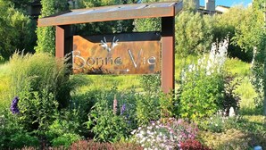 A sign with the name "Bonne Vie" surrounded by a garden with various plants and flowers. - Bonne Vie Condo - Heart of Elkhorn + Resort Amenities (Sun Valley)