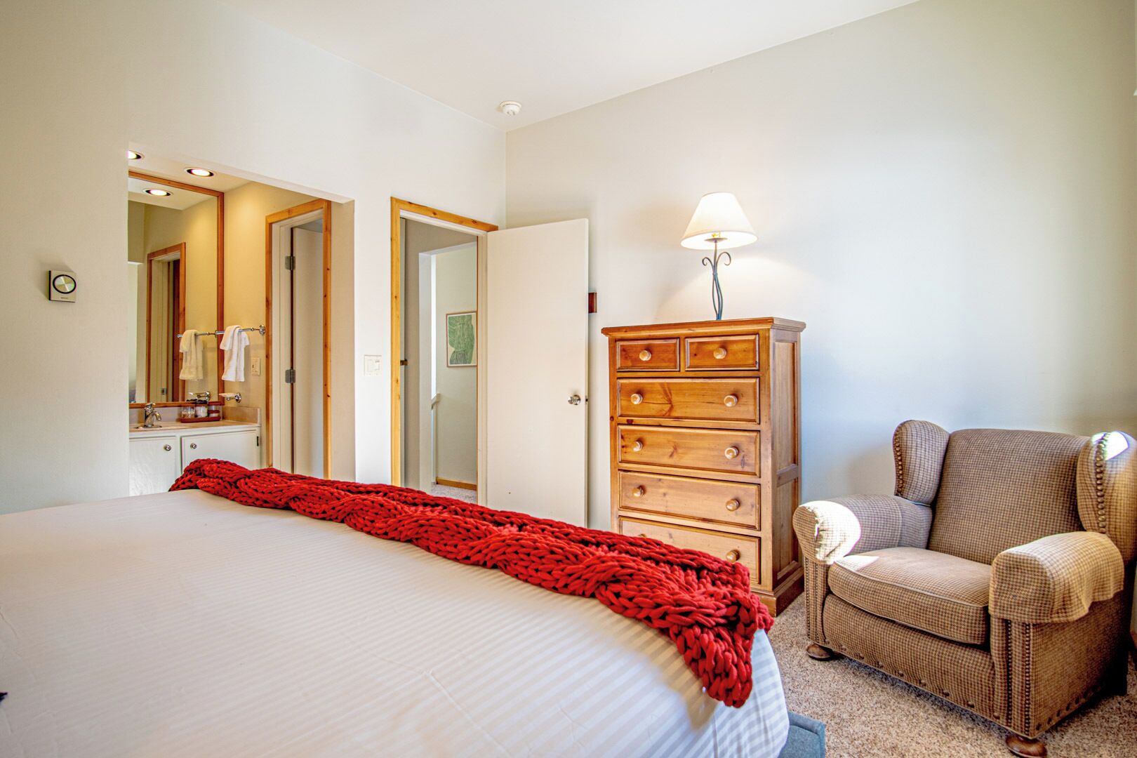 Una habitación de hotel con una cama grande, un aparador de madera, una silla y una lámpara.