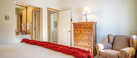 Una habitación de hotel con una cama grande, un aparador de madera, una silla y una lámpara.