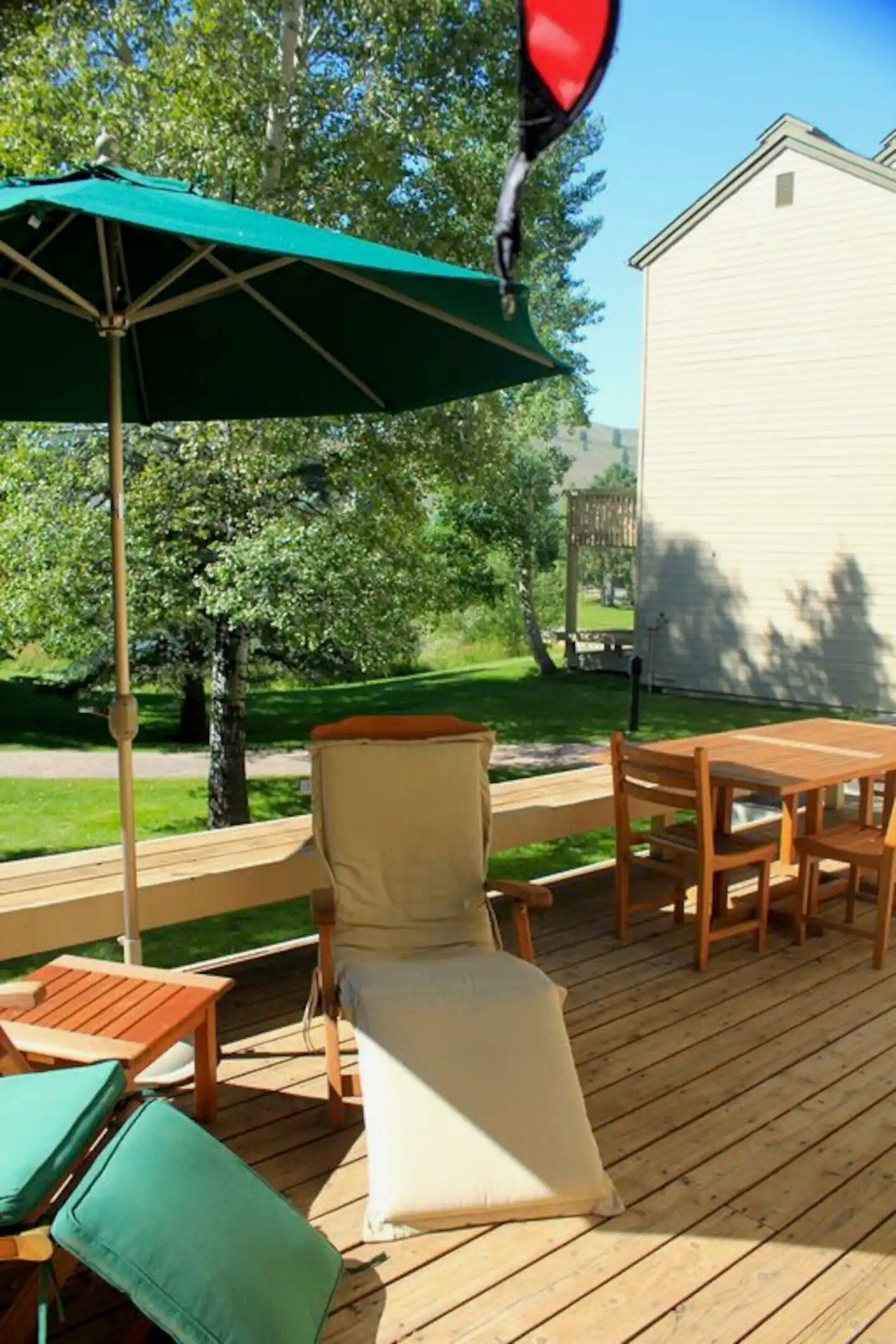 A wooden deck with a green umbrella, a cushioned chair, and a table.