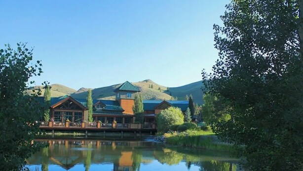 A lodge with a reflection in a lake, surrounded by greenery and hills. - Bonne Vie Condo - Heart of Elkhorn + Resort Amenities (Sun Valley)