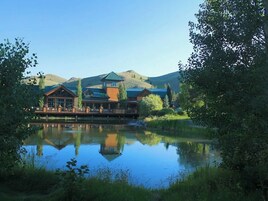 Uma pousada refletida em um lago, cercada por vegetação e colinas.