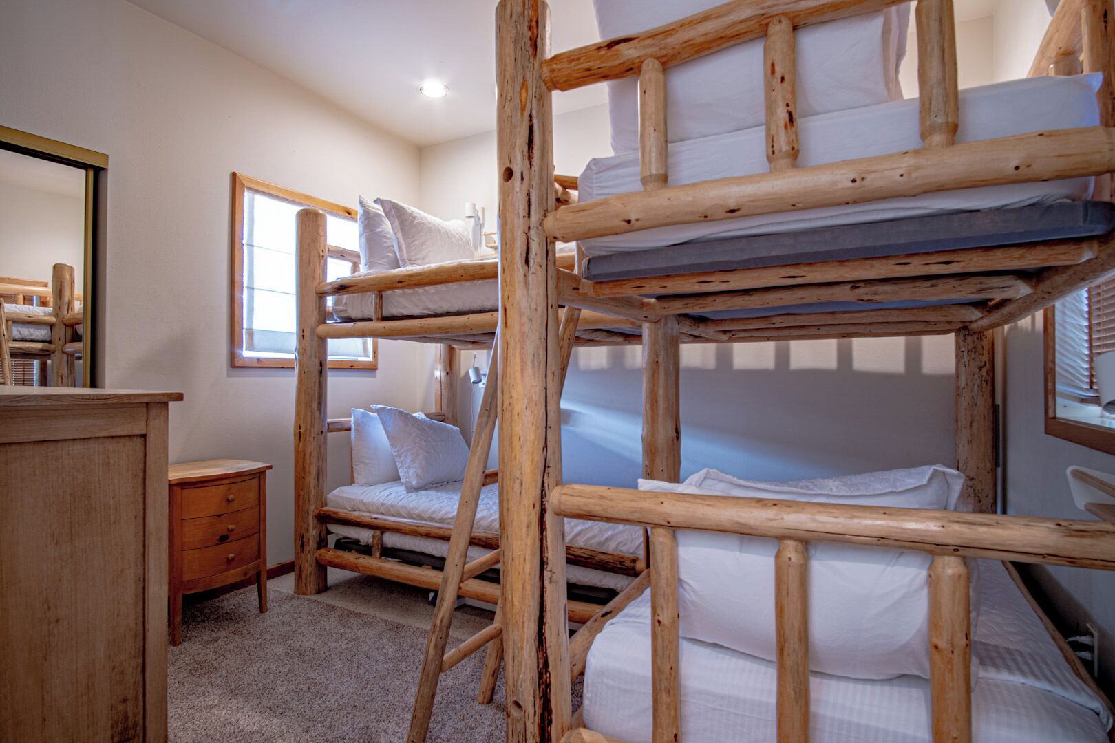 A bunk bed room with a wooden ladder, a small bedside table, and a mirror on the wall.