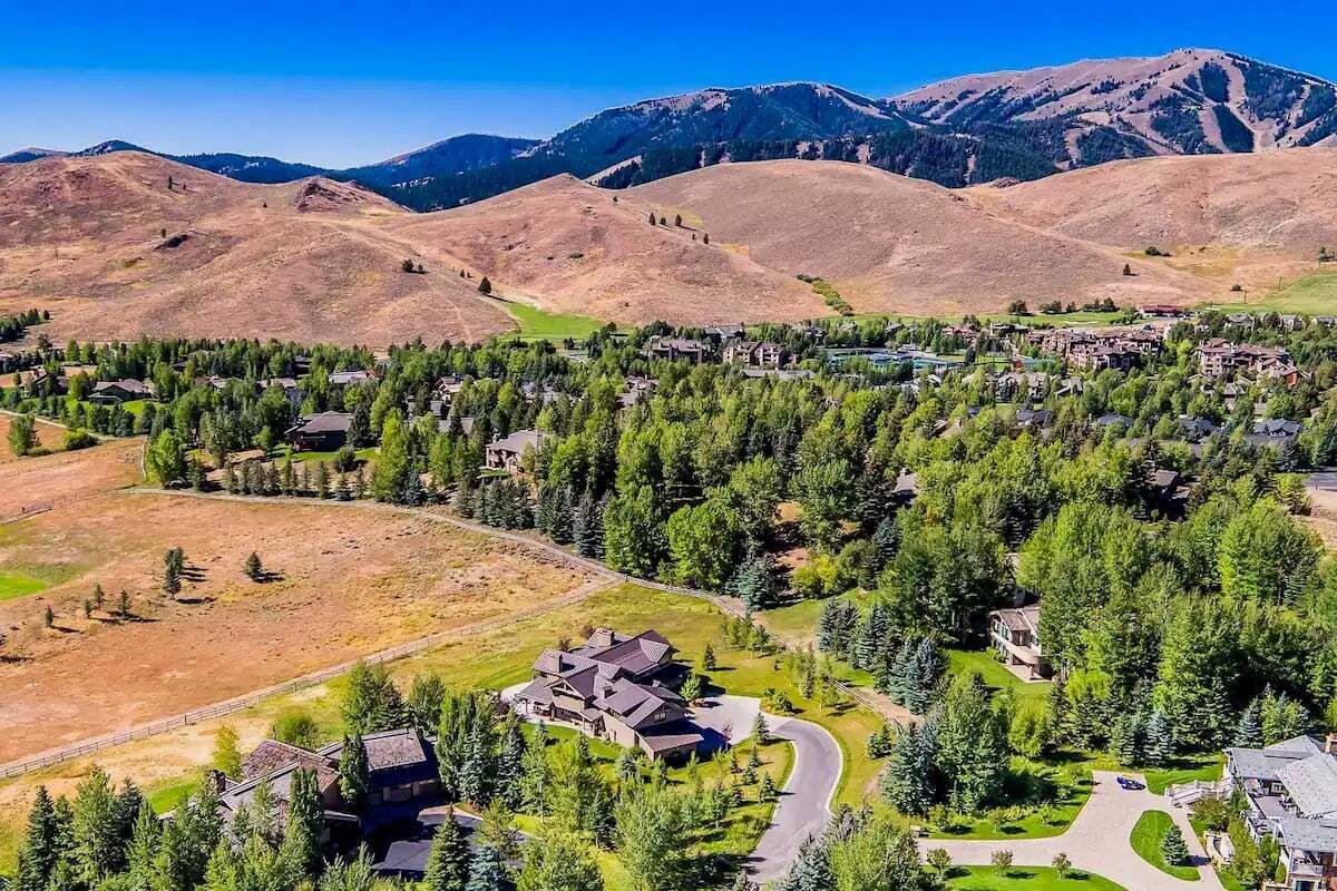 A residential area with houses surrounded by dense forests and mountains in the background.
