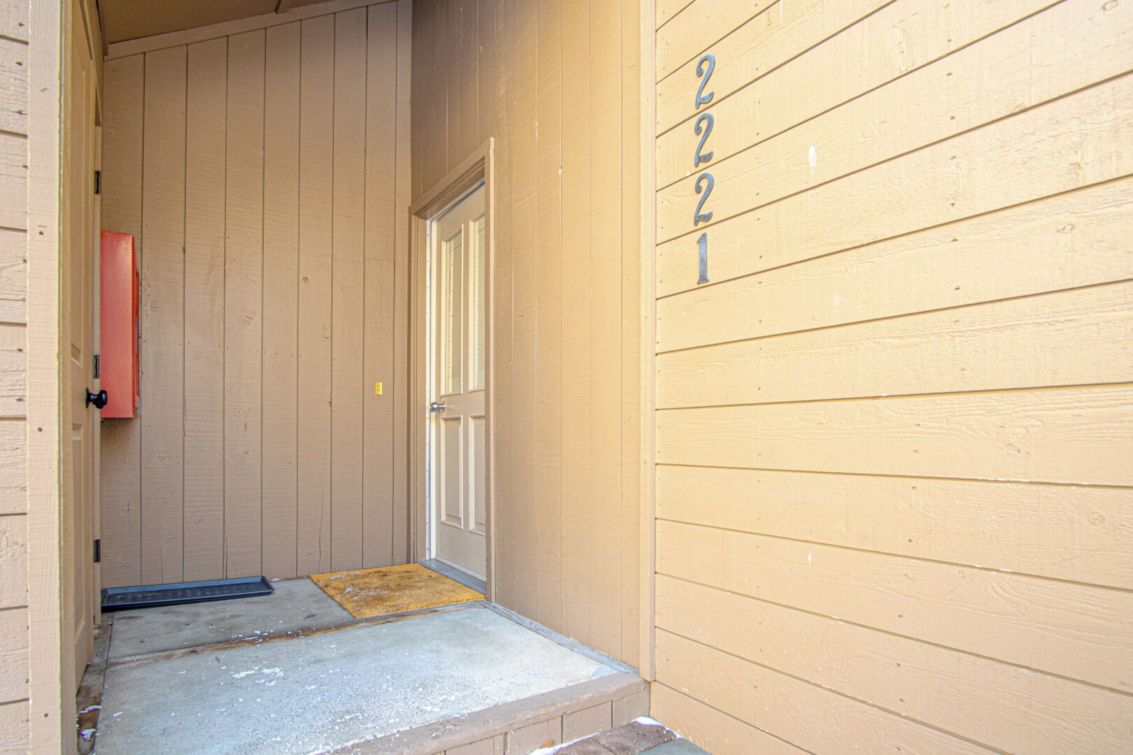 A narrow entrance with a wooden door, a mailbox, and a number '221' on the wall.