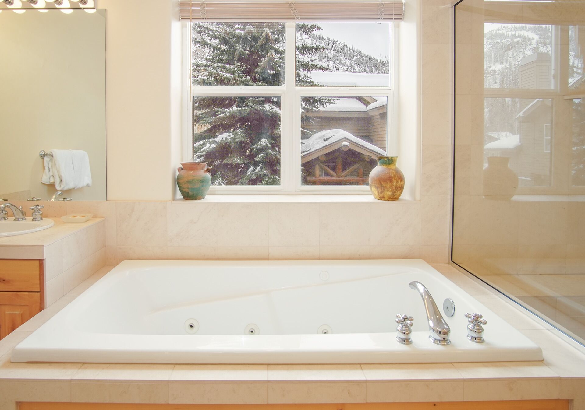 Un baño con una bañera grande, una ventana que ofrece vistas a árboles cubiertos de nieve y un florero en el alféizar.