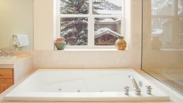 Un baño con una bañera grande, una ventana que ofrece vistas a árboles cubiertos de nieve y un florero en el alféizar.