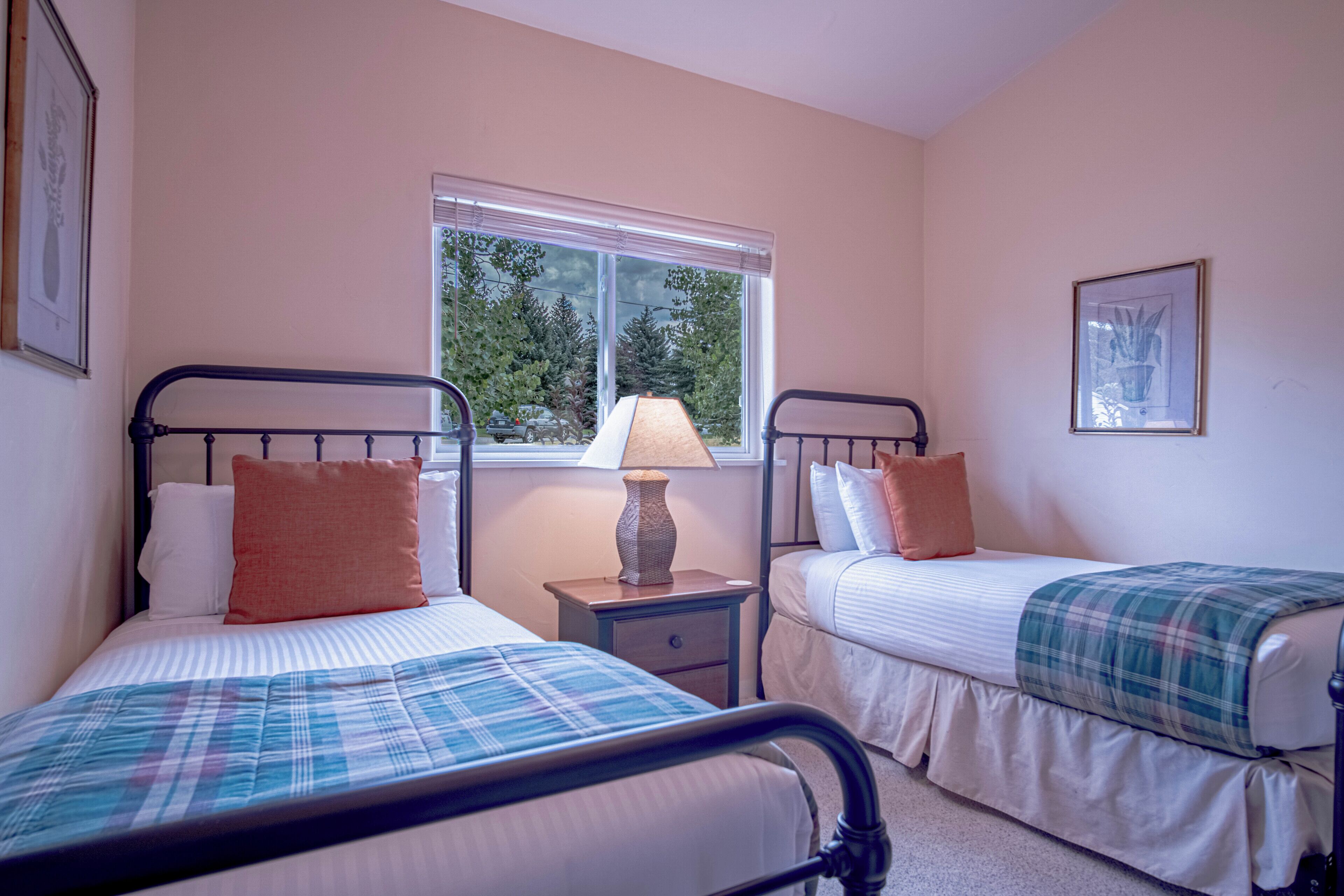 A bedroom with two beds, a nightstand, a window, and a framed picture on the wall.
