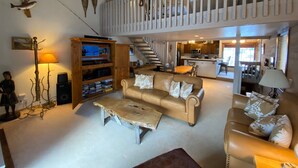 Un vaste espace de vie doté d’un haut plafond, d’un escalier en bois et d’une cuisine située au fond de la pièce.