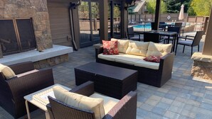 Un espace patio aménagé avec des meubles en osier, une cheminée en pierre et une piscine en arrière-plan.