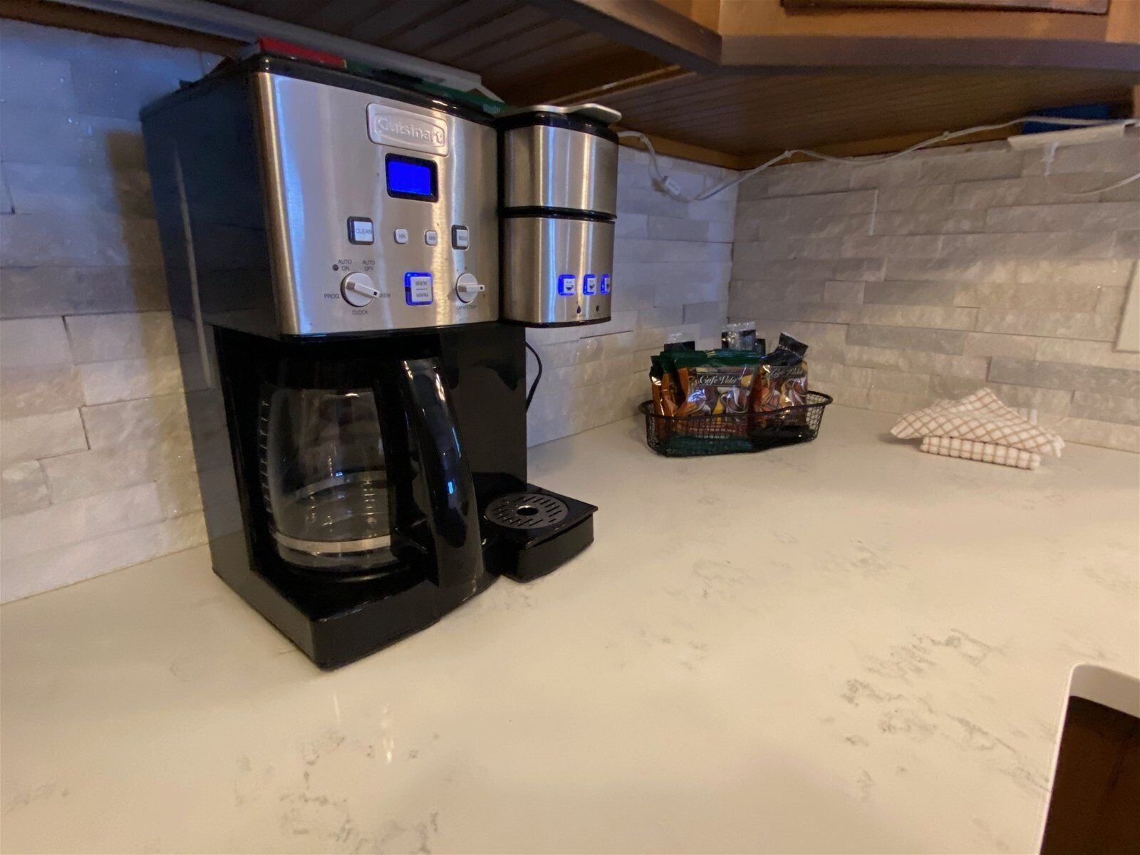 A kitchen with a coffee maker, two stainless steel containers, and a basket of coffee pods.