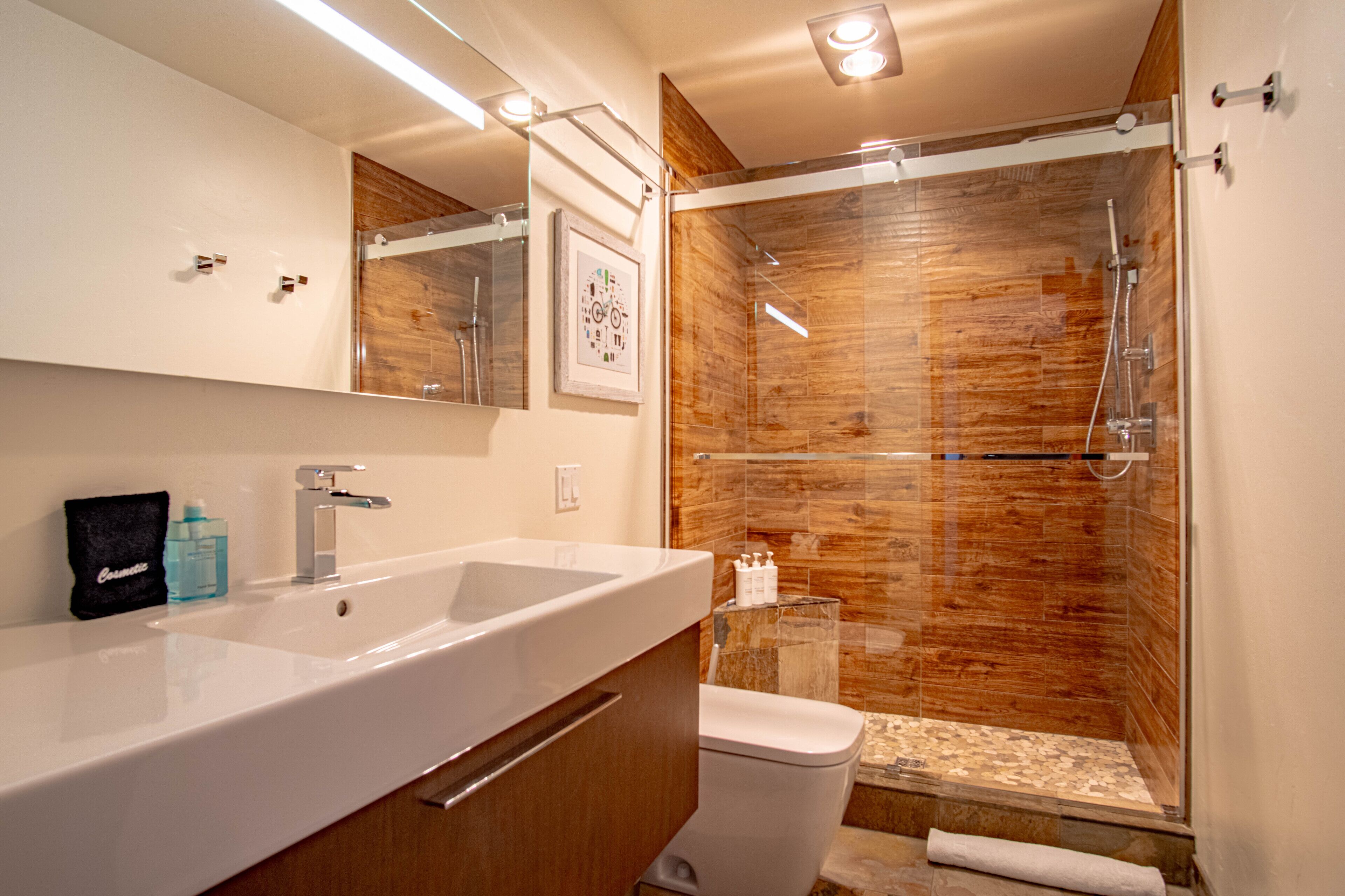 A modern bathroom with a large white sink, a mirror, a toilet, and a glass-enclosed shower area.