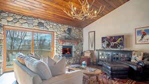 A cozy living room with a stone wall, a fireplace, a large window, and a chandelier. - Ridge Condo - Modern Luxury Condo W/resort Amenities (Sun Valley)