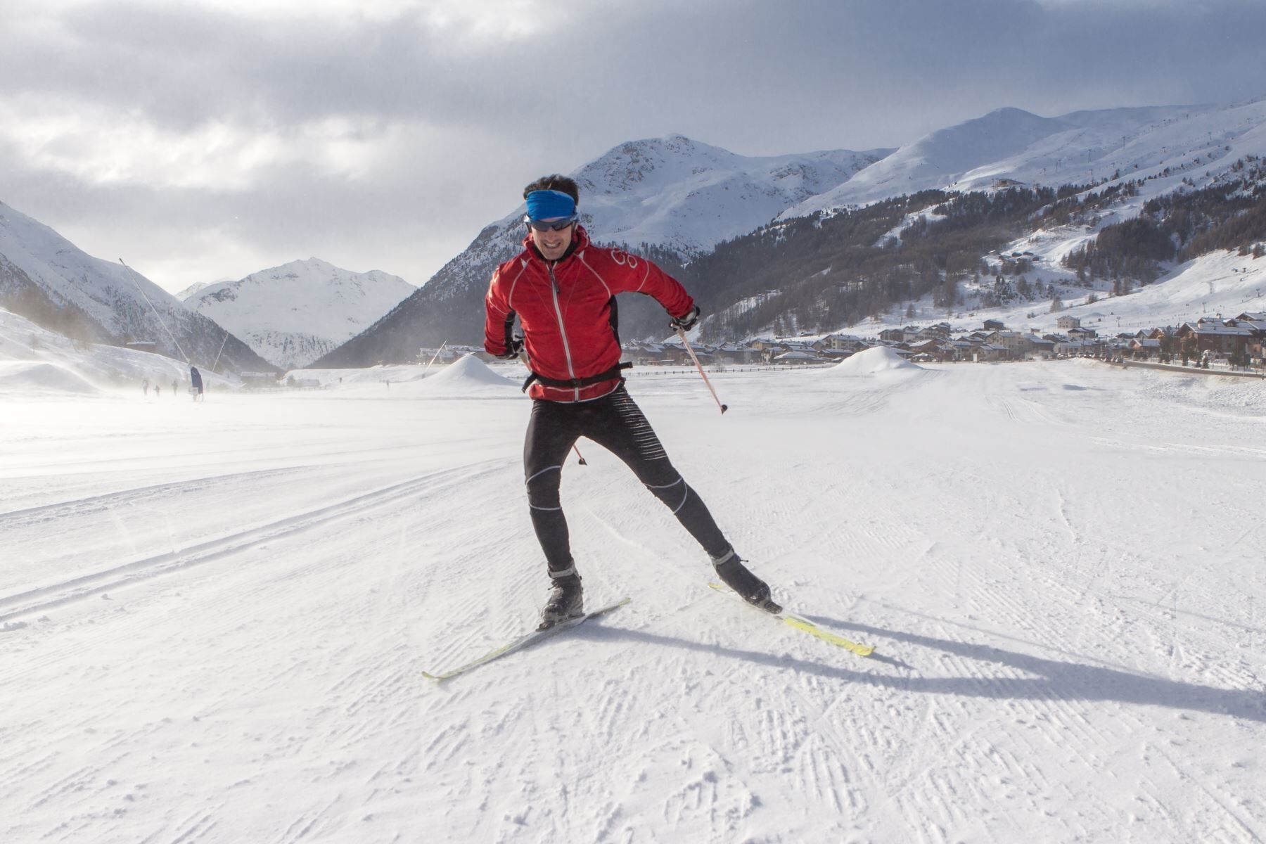 Une personne pratiquant le ski de fond sur une piste enneigée, avec des montagnes en arrière-plan.