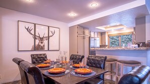 A dining area with a dark wooden table set for six, surrounded by black leather chairs. There are framed deer antlers on the wall above the table. - Ridge Condo - Modern Luxury Condo W/resort Amenities (Sun Valley)