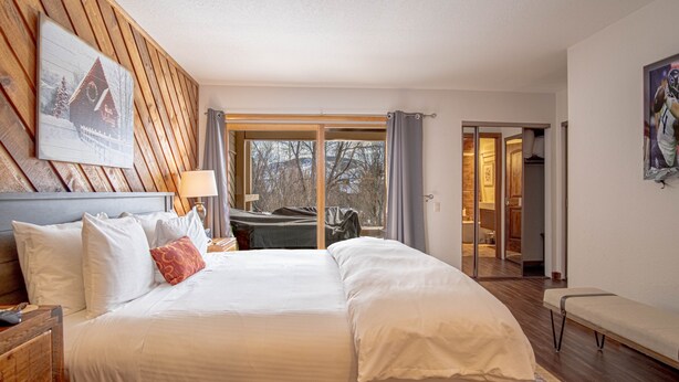 A hotel room with a large bed, wooden headboard, a painting, a bench, and a view of the outdoors. - Ridge Condo - Modern Luxury Condo W/resort Amenities (Sun Valley)