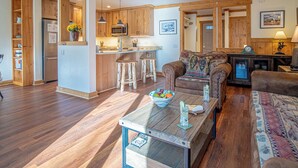 A spacious living area with a wooden floor, a central island with stools, a sofa, and a coffee table with a bowl of fruit. - Sv109 - Walk to Lifts & Town - Hot Tub & Pool (Ketchum)