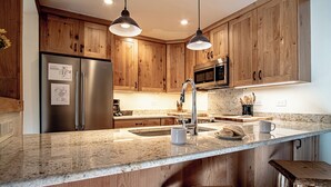 A kitchen with wooden cabinets, stainless steel appliances, granite countertops, and pendant lighting. - Sv109 - Walk to Lifts & Town - Hot Tub & Pool (Ketchum)