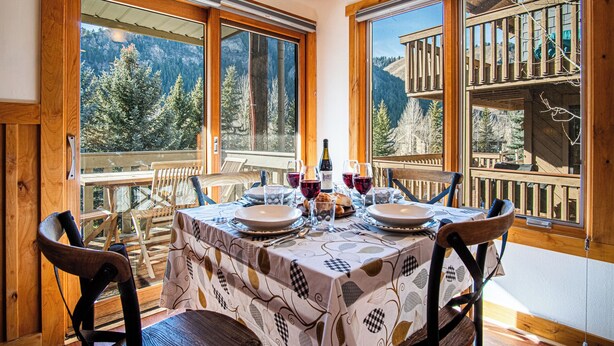 A dining area with a table set for four, large windows offering mountain views, and wooden furniture. - Sv109 - Walk to Lifts & Town - Hot Tub & Pool (Ketchum)