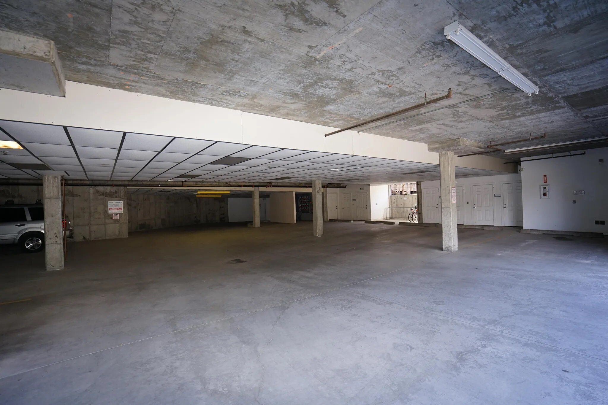 Eine große, leere Parkgarage mit Betonpfeilern, ebener Decke und wenigen Türen.