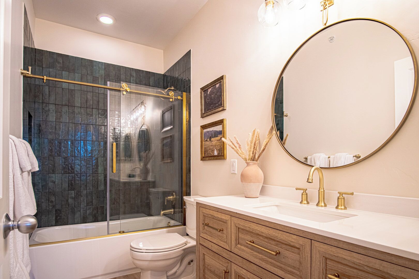 A modern bathroom with a glass-enclosed shower, a round mirror, and a vanity with gold fixtures.