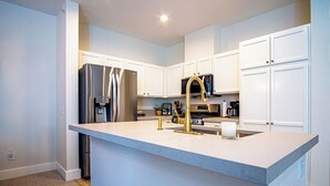 A modern kitchen with white cabinetry, stainless steel appliances, and a central island with a gold faucet. - Snow Star Serenade - Hot Tub + Gym + Walk to Downtown & ski Lifts! (Ketchum)