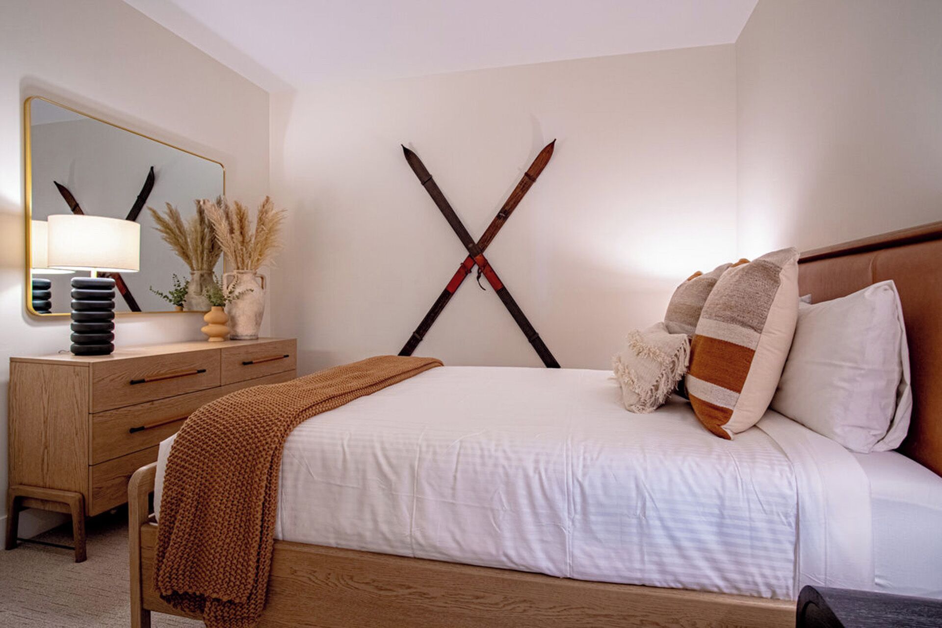 Un dormitorio con una cama, una mesita de noche, una lámpara y un espejo fijado a la pared.