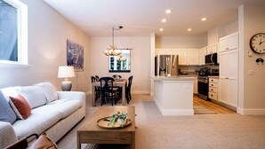 A modern living room with a sofa, dining table, and kitchen area with white cabinets and appliances. - Snow Star Serenade - Hot Tub + Gym + Walk to Downtown & ski Lifts! (Ketchum)