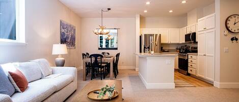 A modern living room with a sofa, dining table, and kitchen area with white cabinets and appliances.
