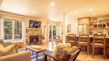 A spacious living room with a stone fireplace, a dining area with wooden chairs, and a kitchen with modern appliances.