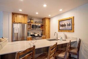 A modern kitchen with a large island, stainless steel appliances, wooden cabinets, and a farmhouse-style sink. - Walk to Lifts & Town - Hot Tub & Pool (Ketchum)