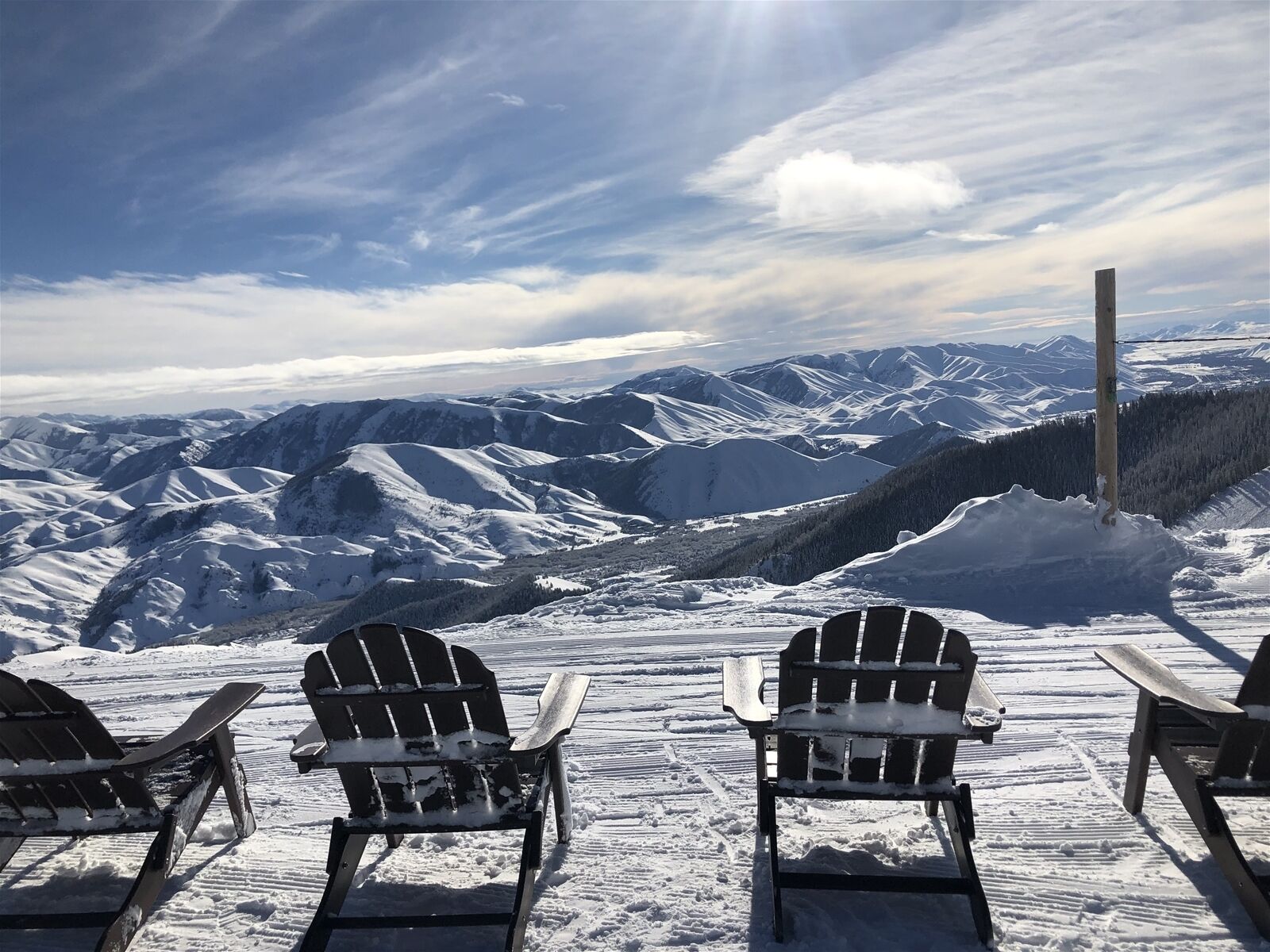Un espace extérieur aménagé avec des sièges, recouvert de neige, et des fauteuils Adirondack disposés face à un paysage montagneux.