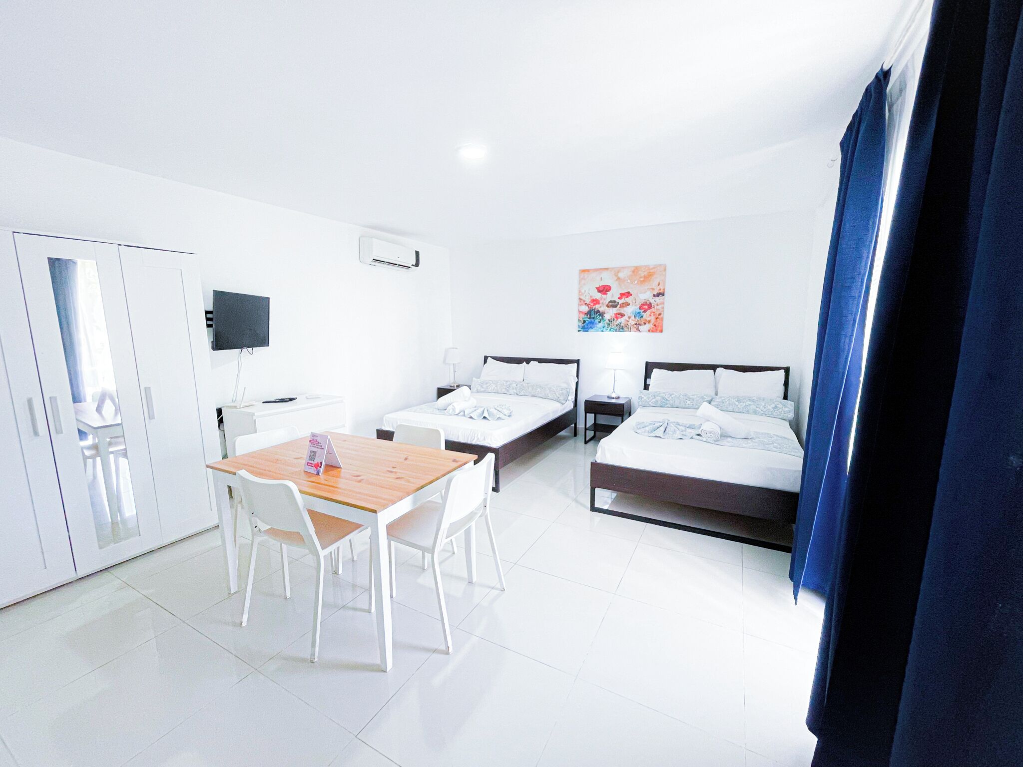 A hotel room with two beds, a desk, a chair, a TV, and a painting on the wall.