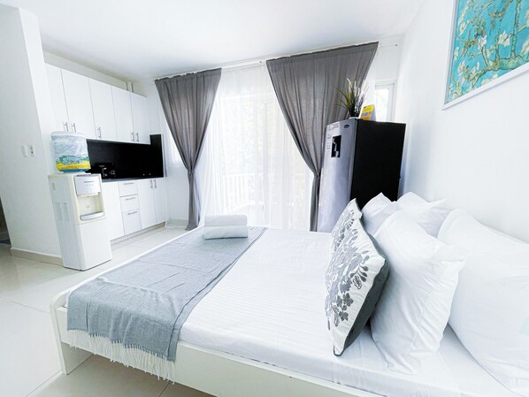 Una camera d'albergo moderna con un letto, una TV a schermo piatto, un minibar e un dispenser d'acqua.