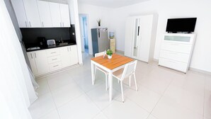 Une cuisine moderne avec des meubles blancs, une table à manger en bois et un téléviseur posé sur un meuble blanc.