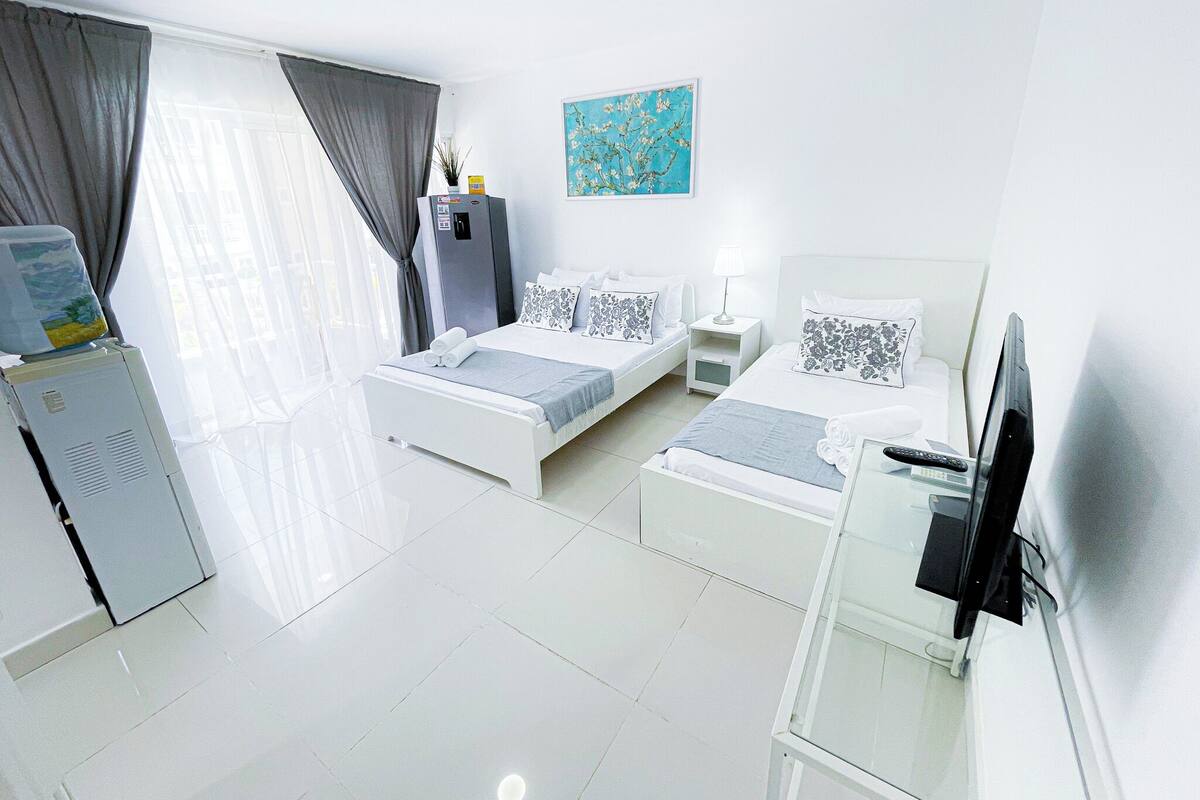 Una habitación de hotel moderna con dos camas individuales, un escritorio, un televisor y un refrigerador.