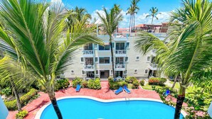 Una piscina rodeada de palmeras y un edificio de varios pisos con balcones.