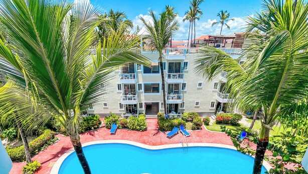 Une piscine entourée de palmiers et un immeuble à plusieurs étages doté de balcons.