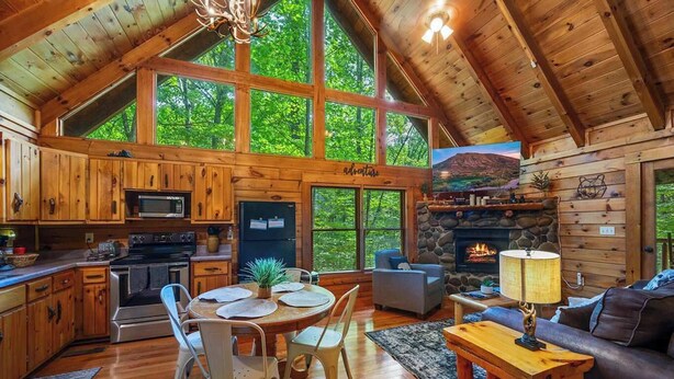A cabin with a kitchen, dining area, and living room, featuring wooden walls, large windows, and a stone fireplace. - Secluded Cabin for 4 w/ Private Hot Tub & Jacuzzi! (Sevierville)