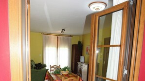 Un coin repas avec une table dressée pour quatre personnes, un canapé vert et une cuisine en arrière-plan.