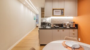 Et moderne køkken med en central ø, indbyggede hårde hvidevarer og et spiseområde med et bord dækket til to personer.