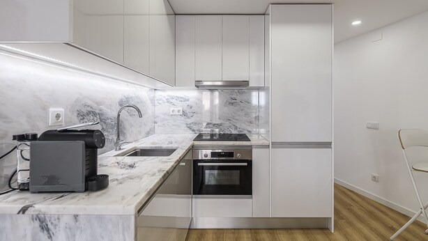 Una cocina moderna con armarios blancos, horno integrado y encimera de mármol.