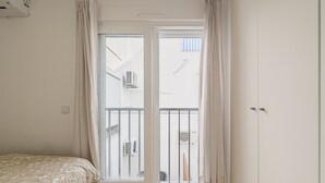 Un dormitorio con cama, puerta corrediza de vidrio a un balcón y un armario blanco.