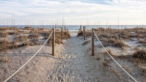 A sandy beach path leading to the ocean, with wooden posts and ropes guiding the way. - Steps to beach with views galore! (Emerald Isle)