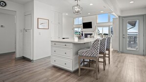 A modern kitchen with white cabinetry, a built-in island, and a dining area with patterned chairs. - Steps to beach with views galore! (Emerald Isle)